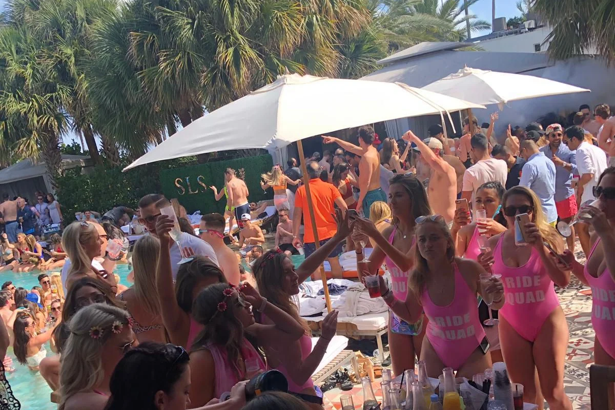 Guests celebrating poolside at the SLS pool party in Miami Beach, with SLS signage behind the crowd